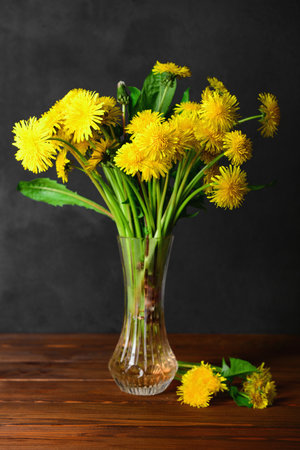 Vase with beautiful dandelion flowers on wooden table against dark backgroundの写真素材