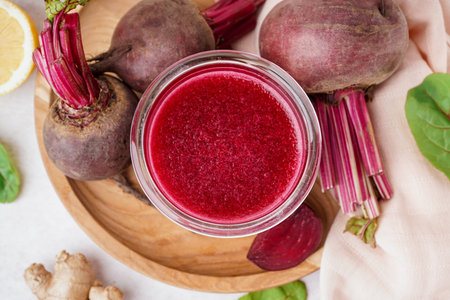 Glass of fresh beetroot juice and vegetables on light background