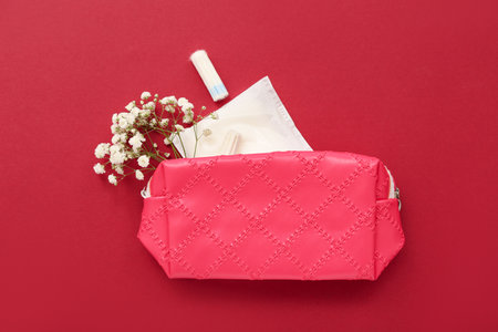 Lady's cosmetic bag with tampons, menstrual pad and flowers on dark red backgroundの写真素材