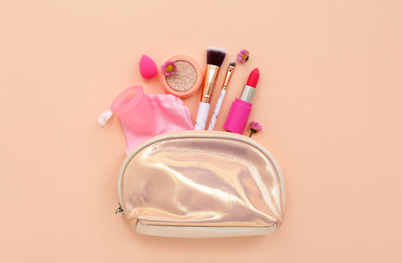 Lady's cosmetic bag with makeup products, menstrual cup and sponge on pale orange backgroundの写真素材
