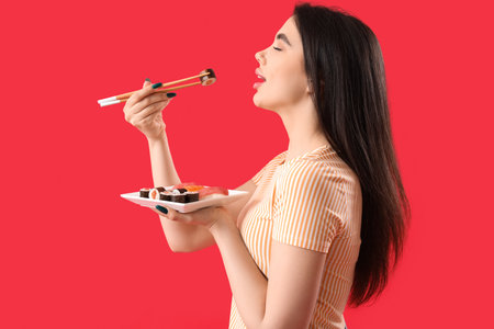 Young woman eating sushi rolls on red backgroundの写真素材
