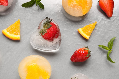 Fresh strawberry and pieces of orange frozen in ice on gray backgroundの写真素材