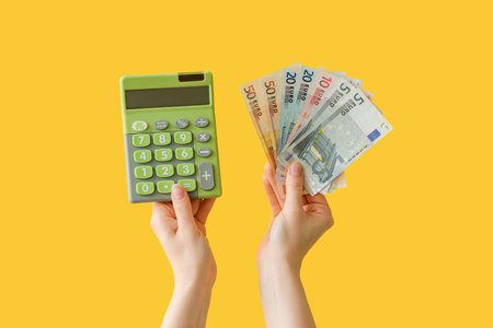 Woman with euro banknotes and calculator on yellow backgroundの写真素材