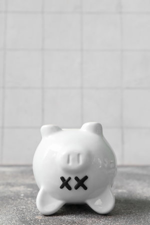 Piggy bank with closed eyes on grunge table near white tile background. concept of bankruptcyの写真素材