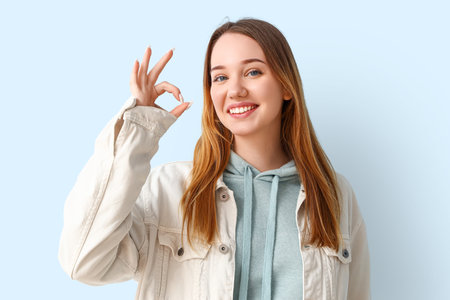 Beautiful young woman showing OK on blue backgroundの写真素材