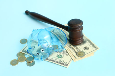 Broken plastic piggy bank with judge gavel and money on blue background. bankruptcy conceptの写真素材