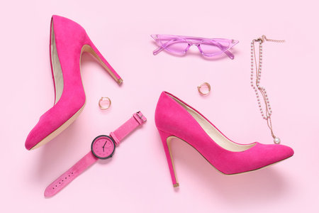 Sunglasses, pair of high heels, wristwatch and jewelery on pink backgroundの写真素材