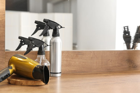 Hairdryer and bottles of spray on table in beauty salonの写真素材