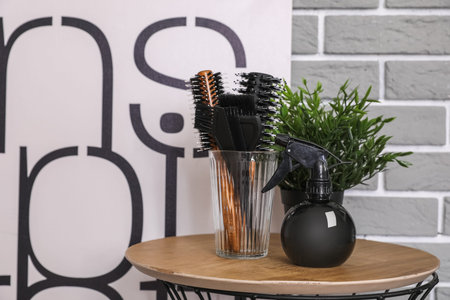 Bottle of spray and different brushes on table near gray brick wall in salon