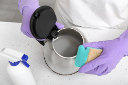 Woman in purple rubber gloves cleaning electric kettle with spongeの写真素材