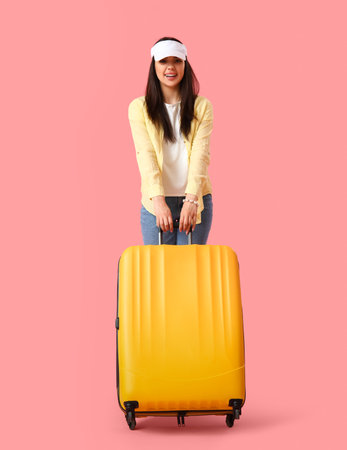 Young woman with suitcase on pink backgroundの写真素材