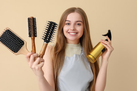 Female hairdresser with brushes and spray on beige backgroundの写真素材