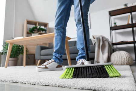 Young man sweeping carpet with broom at home, closeupの写真素材