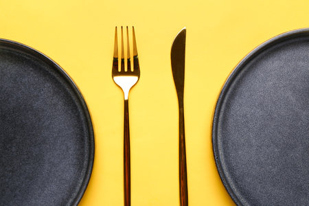 Table setting with clean plates and cutlery on yellow backgroundの写真素材