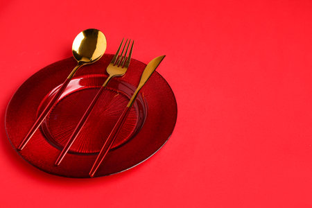 Table setting with clean plate and cutlery on red backgroundの写真素材
