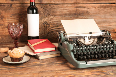 Vintage typewriter, bottle of wine, glass, muffin and books on wooden tableの写真素材