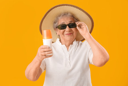 Senior woman with sunscreen cream on orange backgroundの写真素材
