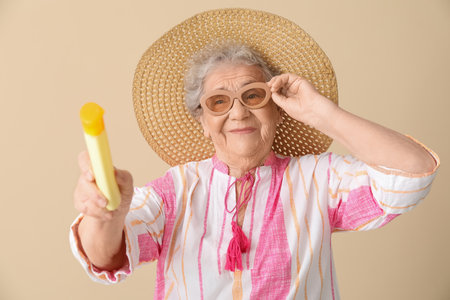 Senior woman with sunscreen cream on beige backgroundの写真素材