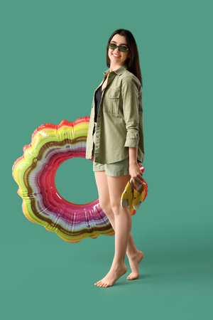 Young woman with flip-flops and inflatable ring on green background