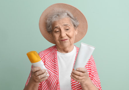 Senior woman with sunscreen cream on green background, closeupの写真素材