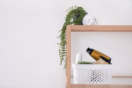 Shelving unit with bath accessories and houseplant near light wallの写真素材