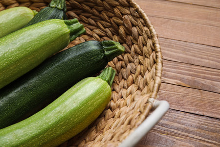 Wicker basket with fresh green zucchini on wooden backgroundの写真素材