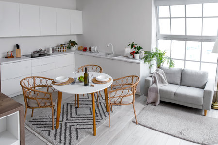 Interior of light open plan kitchen with served dining table and gray sofaの写真素材