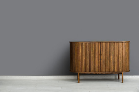Stylish wooden chest of drawers near gray wall in roomの写真素材
