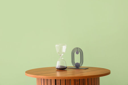 Wooden coffee table with hourglass and decorative figure near green wall