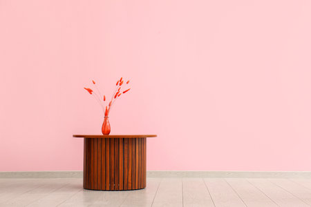 Wooden coffee table with red lagurus grass in vase near pink wallの写真素材