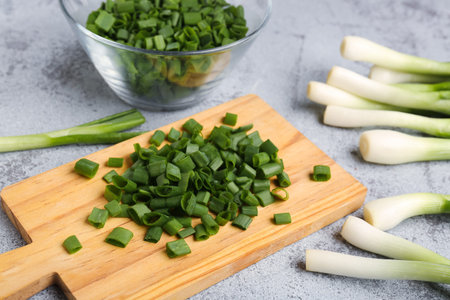 Board and bowl with slices of fresh green onion on gray background