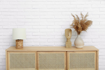 Wooden chest of drawers with lamp and pampas grass near light brick wall in roomの写真素材