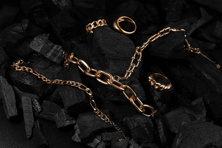 Beautiful chain bracelets and rings on black charcoal, closeup