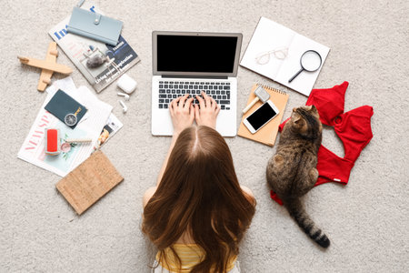 Woman with Scottish fold cat and traveling accessories using laptop on beige carpet, top viewの写真素材