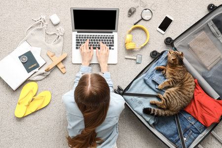 Woman with Scottish fold cat and traveling accessories using laptop on beige carpet, top viewの写真素材
