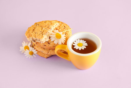 Cup of natural chamomile tea with cookies and flowers on pink backgroundの写真素材