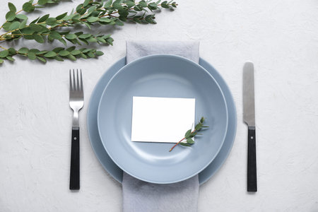 Stylish table setting with blank card and plant branches on white textured background