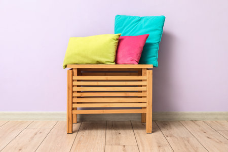 Stylish pillows on wooden drawer near lilac wallの写真素材