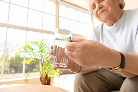 Senior woman with pill and glass of water at home, closeupの写真素材