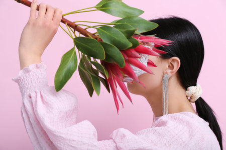 Profile of beautiful young woman wearing stylish earrings with protea flower near pink wallの写真素材