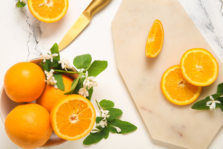 Board and bowl of oranges with blooming branches on white tableの写真素材