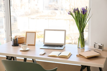 Modern workplace with laptop, notebooks, coffee cup and flowers in officeの写真素材
