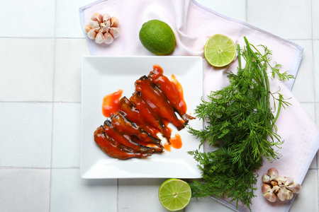 Plate with canned fish in tomato sauce, lime, garlic and dill on white tiled table