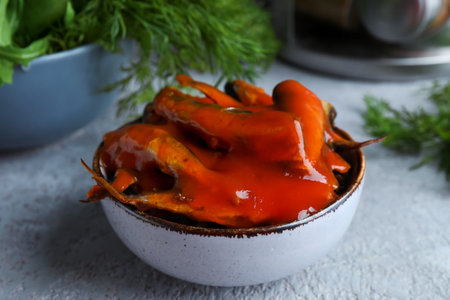 Bowl with canned fish in tomato sauce on gray table