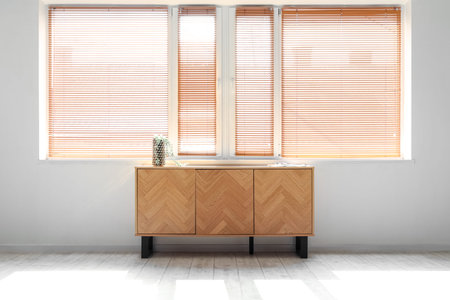 Stylish wooden cabinet near window with blinds