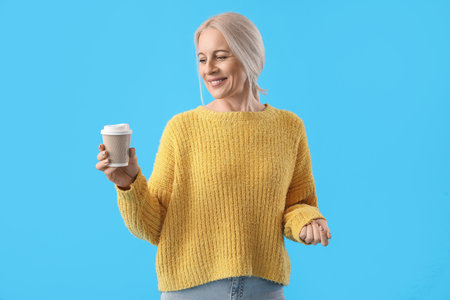 Mature woman with cup of coffee on blue backgroundの写真素材