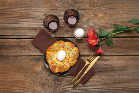 Plate with tasty Italian Easter bread, eggs, glasses and alstroemeria flowers on wooden background
