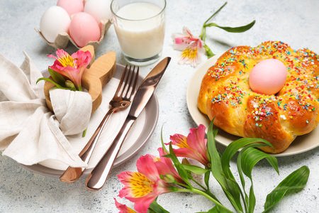 Table setting with tasty Italian Easter bread, eggs, glass of milk and alstroemeria flowers on light backgroundの写真素材