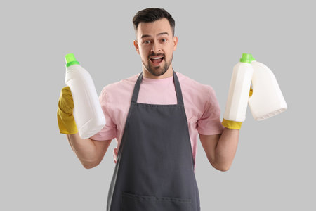 Male janitor with bottles of detergent on gray backgroundの写真素材