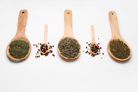Wooden spoons with dried herbs and peppercorns on light backgroundの写真素材